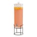 A Cal-Mil glass beverage dispenser with a black wire base filled with orange juice and lemons.