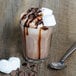 A Duralex glass of chocolate milkshake with marshmallows and a spoon.