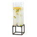A Cal-Mil square drink dispenser with an ice chamber and black metal base full of water with lemon and lime slices.