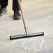 A person using a Lavex black neoprene floor squeegee to clean the floor.