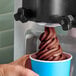 A person holding a cup of chocolate soft serve ice cream.