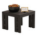 A black wood display riser with a bowl of olives and peppers on a small table.