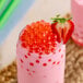 A glass of pink milkshake with Fanale strawberry popping boba and a strawberry slice on the rim.