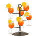 A black wire Cal-Mil cocktail tree with glasses of orange juice and orange slices on it.