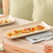 A rectangular beige porcelain platter with a slightly raised edge, shown holding a plated appetizer.