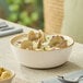 A round beige porcelain bowl filled with clam chowder, shown on a dining table.
