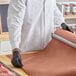 A roll of pink or peach butcher paper being unrolled on a countertop by a person wearing black gloves and a white coat.