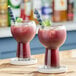 Two glasses of red Acai berry cocktail garnished with blueberries and mint leaves on a wooden bar.