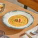 A round gray porcelain wide rim bowl filled with creamy soup and garnished with herbs and seafood.
