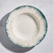 A round gray porcelain wide rim bowl with a speckled design and blue-green edge.