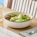 A round gray porcelain bowl filled with salad, placed on a wooden table.