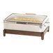 A stainless steel chafer with food inside on a table with a wood and stainless steel stand.