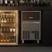 A Scotsman undercounter gourmet cube ice machine in a bar with a refrigerator full of bottles.