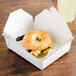 A bagel sandwich in a white Fold-Pak take-out box.