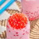 A glass of pink bubble tea with red cherry bursting boba.