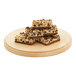A stack of brownies with nuts on top on a wooden plate.