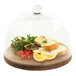 A round walnut display stand with bread and cheese under a glass dome.