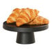 A Cal-Mil black melamine cake pedestal with croissants on it.