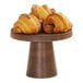 A round wooden table with croissants on a Cal-Mil walnut cake pedestal.