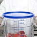 A person holding a Carlisle blue food storage container lid filled with apples.