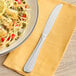 An Acopa stainless steel dinner knife on a plate of food.