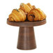 A round wooden table with a Cal-Mil walnut cake pedestal holding croissants.