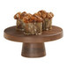 A Cal-Mil round walnut melamine cake pedestal with three cakes on it.