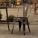 A metal outdoor cafe chair with a distressed copper finish and a curved backrest.