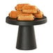 A black round table with a Cal-Mil black melamine cake pedestal holding a pile of pastries.