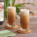 A pair of tall glasses filled with a frothy, brown soda beverage on woven coasters.
