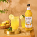 A bottle of Monin Pineapple Yuzu flavoring syrup next to a glass of lemonade with lemon slices.