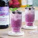Two glasses of Monin purple liquid with mint leaves and berries.