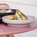 A Cal-Mil taupe melamine bowl/plate with a sandwich and salad on it on a table in a deli.