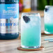 A glass of Monin Berry Blue drink with a straw and a berry in it.