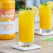 A close up of a glass of yellow Monin Brilliance Starfruit Natural Energy drink with lemon slices and mint leaves.