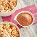 A bowl of Kickin' Cajun popcorn seasoning next to bowls of popcorn on a pink napkin.
