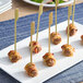 A plate with Cuisine Innovations Bacon Wrapped Wagyu and Gorgonzola Skewers on sticks.