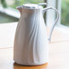 A white Service Ideas Twist 'N' Serv coffee carafe on a table with a handle.