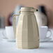 A white Service Ideas insulated coffee carafe on a table next to two white cups.
