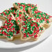 A plate of Christmas tree-shaped sugar cookies decorated with white icing and red and green holiday sprinkles.