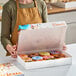 A woman holding a Southern Champion multicolor donut box on a bakery display counter.