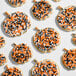A group of pumpkin-shaped cookies decorated with white icing and orange and black Halloween sprinkles.
