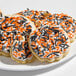 A plate of pumpkin-shaped sugar cookies decorated with white icing and orange and black Halloween sprinkles.