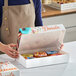 A woman holding a white "Delicious" donut box on a bakery counter.