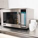 A Sharp stainless steel commercial microwave on a counter with two white mugs.