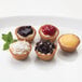 A white plate with four mini assorted cheesecakes on it.
