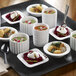 A tray of Solia round white fluted porcelain mini dishes with bowls of food and a white cup of soup.