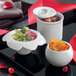 A black tray holding a group of white Solia porcelain mini dishes with food in them.