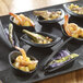 A table with a tray of shrimp and vegetables in black Solia Mini dishes.