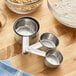 A set of four stainless steel measuring cups on a wooden surface.